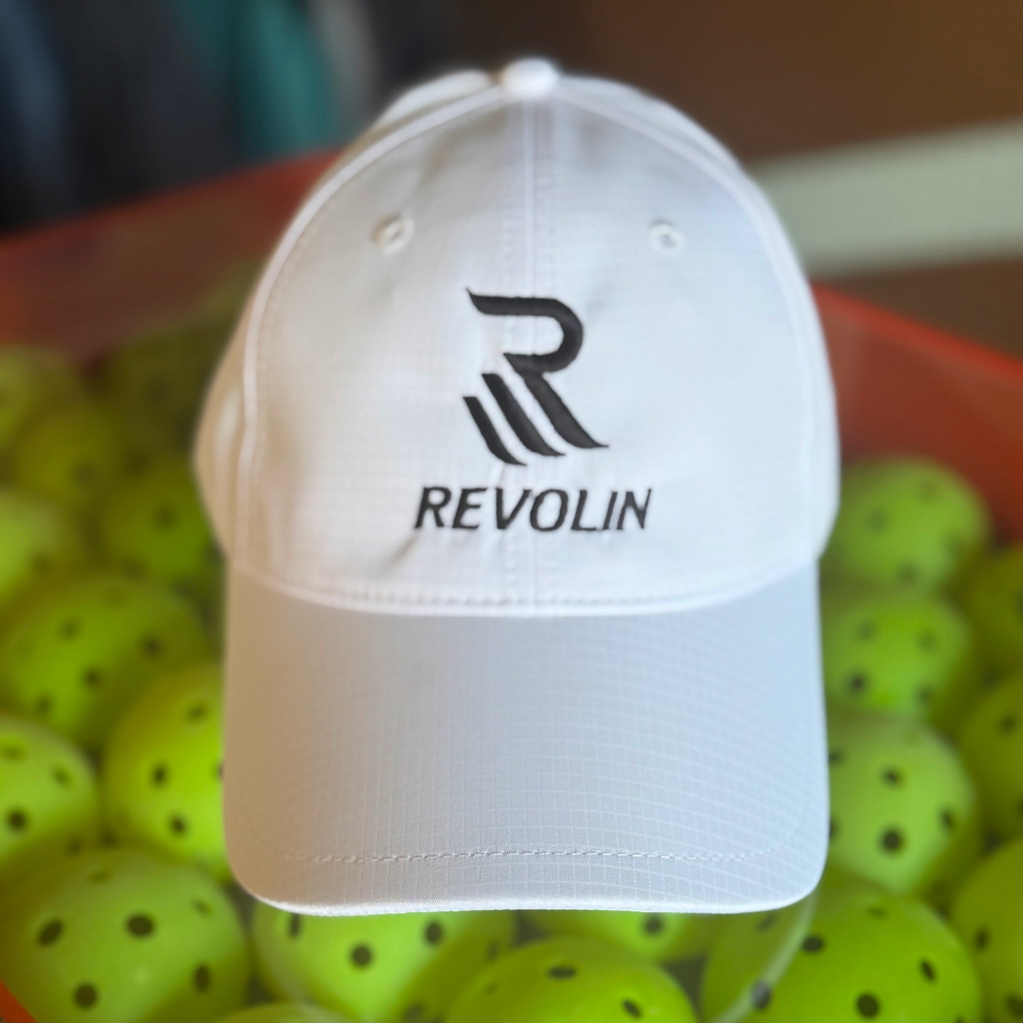White cap with Revolin logo on a background of pickleball balls