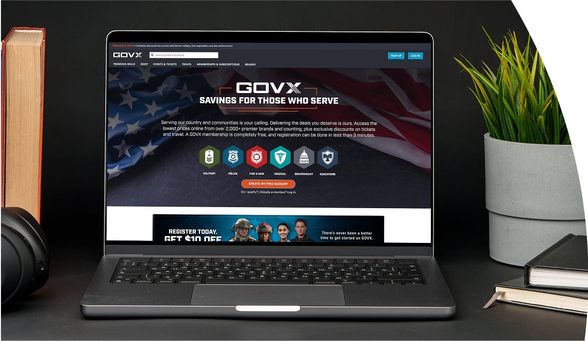 Laptop displaying the GOVX website on a desk with books, headphones, and a plant.