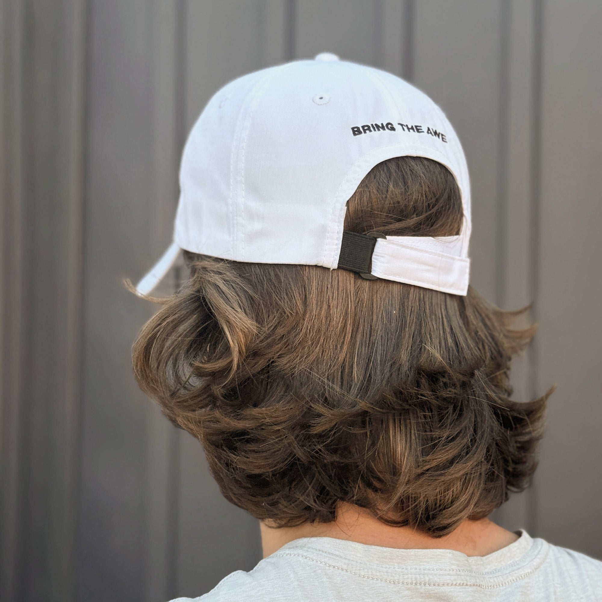 Person wearing a white cap with 'BRING THE AWE' text, facing away from the camera.