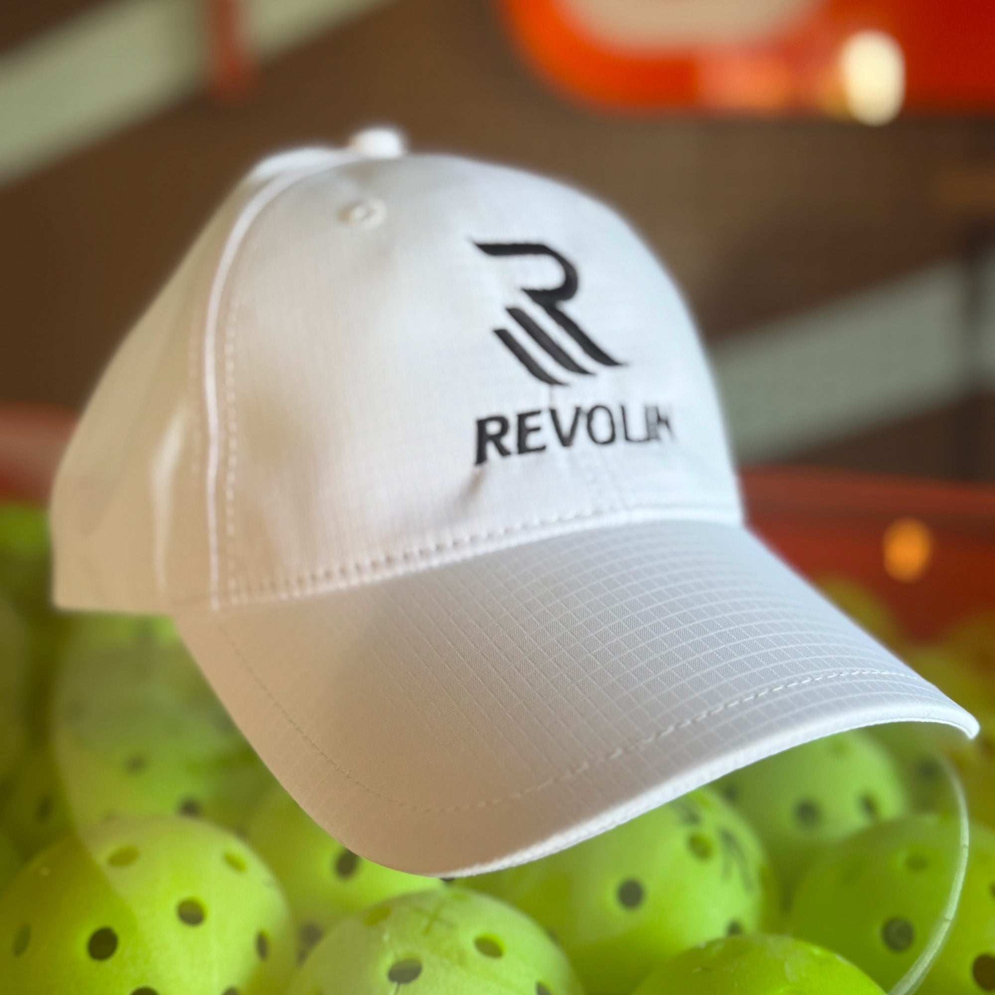 White cap with 'Revolin' logo on a background of pickleball balls
